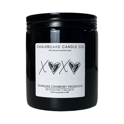 A black jar of Chalkboard Candle Co. sparkling cranberry Prosecco scent candle, with a white label featuring black hearts and the letters 'X' in the center, on a white background.