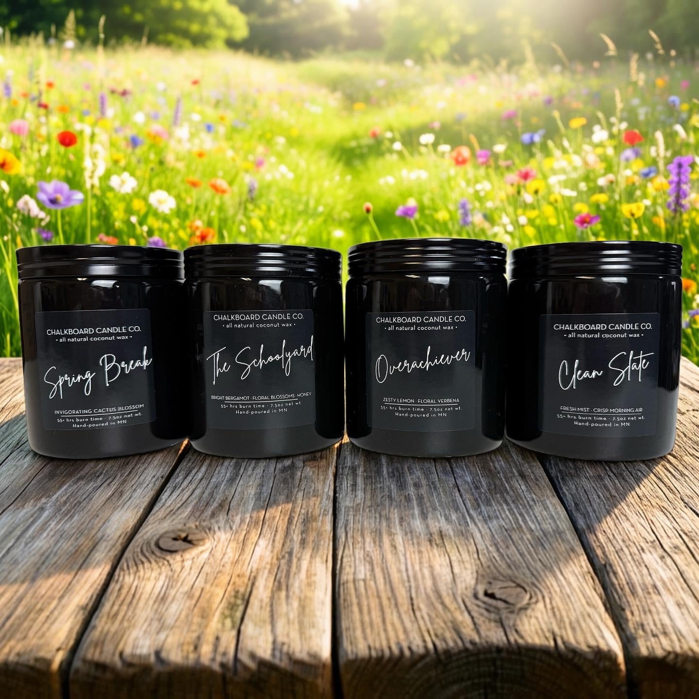 Four black Chalkboard Candle Co. jars labeled Spring Break, The Schoolyard, Overachiever, and Clean Slate on a wooden table.
