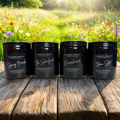 Four black Chalkboard Candle Co. jars labeled Spring Break, The Schoolyard, Overachiever, and Clean Slate on a wooden table.