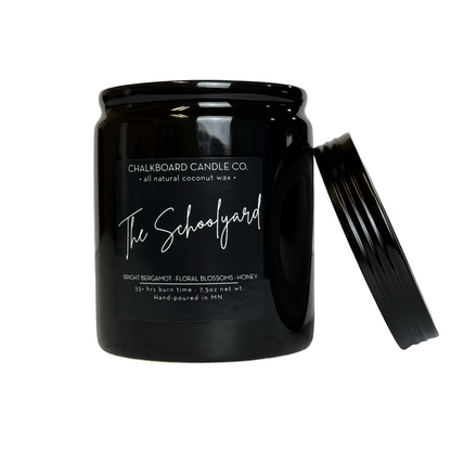 Black glass candle jar labeled Chalkboard Candle Co. The Schoolyard — Bright Bergamot, Floral Blossoms, Honey; hand-poured MN