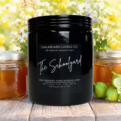 Black candle jar labeled 'The Schoolyard' (Chalkboard Candle Co., all natural coconut wax) with honey jars and limes.